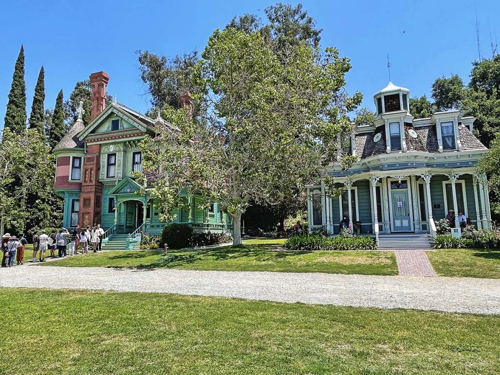 Two old historical homes. A group of people are lined up to enter the house on the left.